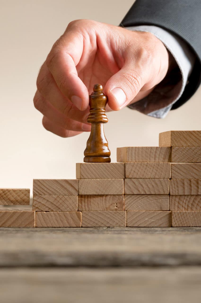 Business success and promotion concept with a businessman moving a chess piece up a series of steps formed by building blocks being put in place by his team in a close up view.